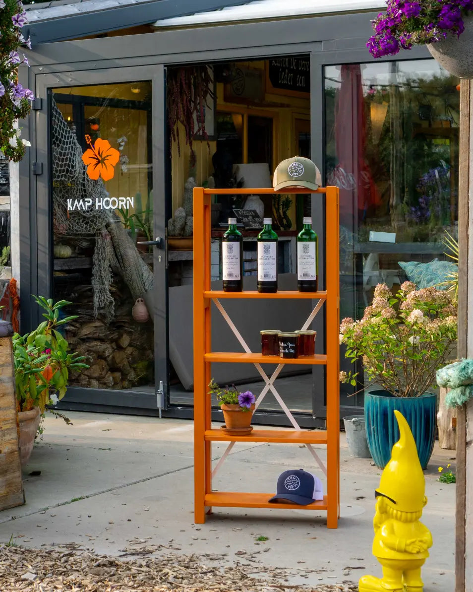 Oranje houten rek met flessen, glazen, petten en planten voor glazen deur van winkel met oranje bloemsticker