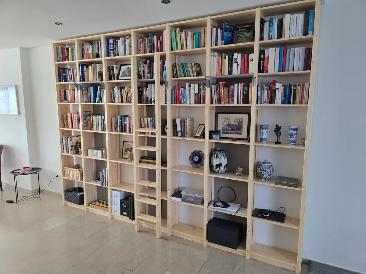 Grote houten boekenkast met boeken, decoraties en een houten ladder in een lichte, rustige woonruimte
