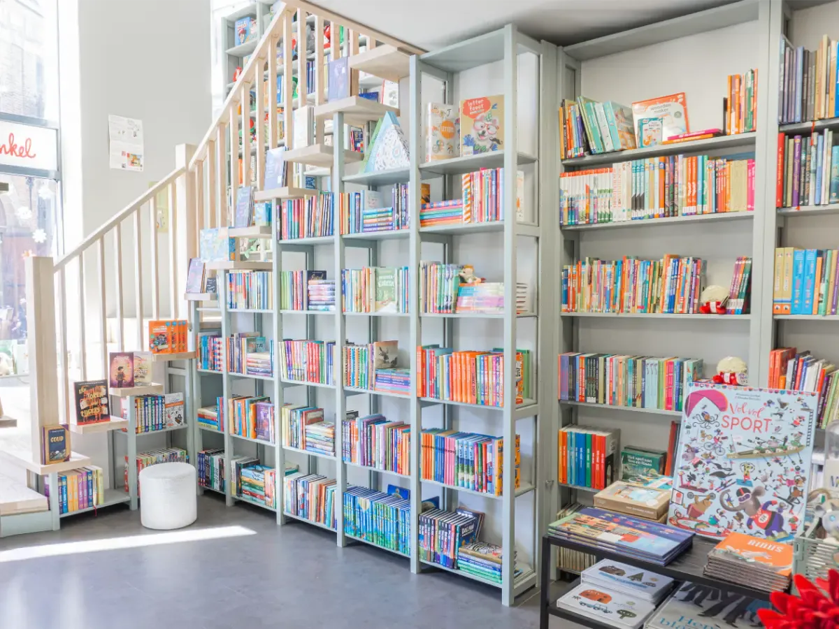 Licht interieur met hoge planken vol kinderboeken en een tafeltje met diverse boeken en tijdschriften erbij