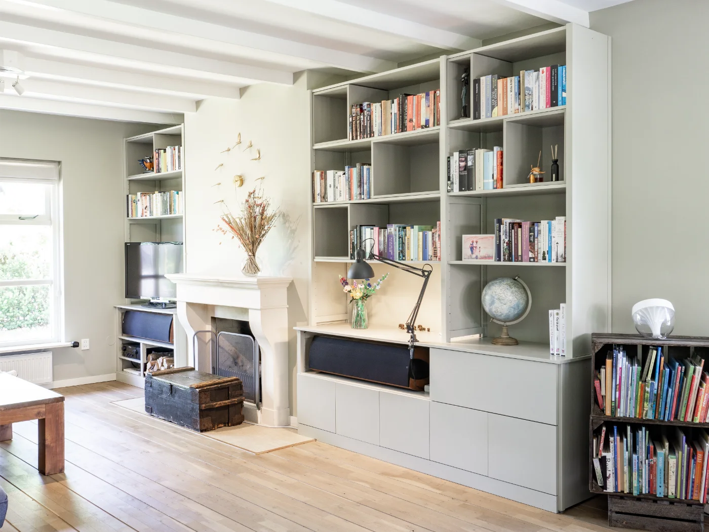 Lichte woonkamer met houten vloer, ingebouwde boekenkasten, open haard en venster met natuurlijk licht