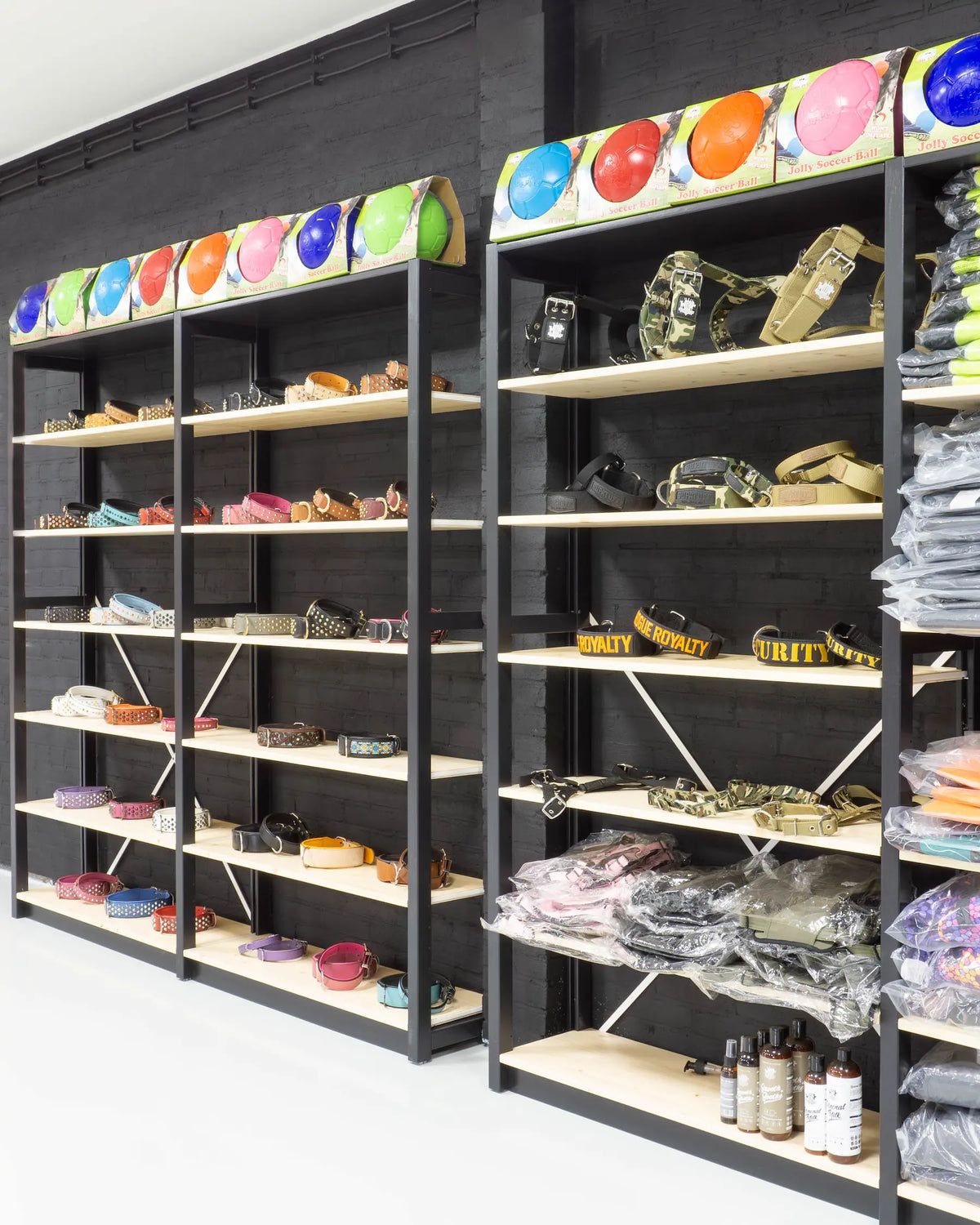 Zwarte metalen rekken tegen donkere muur met diverse riemen, halsbanden en verpakte kledingartikelen erop en ernaast.