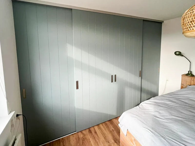 eenvoudige slaapkamer met een grote grijze schuifdeurkast en een bed met een grijs dekbed naast een houten nachtkastje